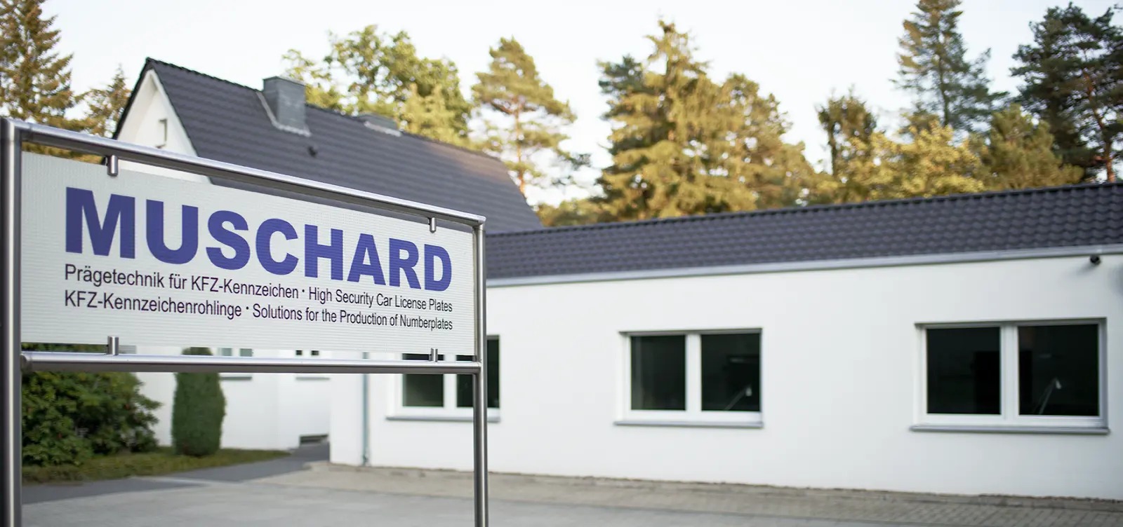 Einfahrt zur Firma Muschard, auf der linken Seite Ein großes Schild mit dem Firmennamen
